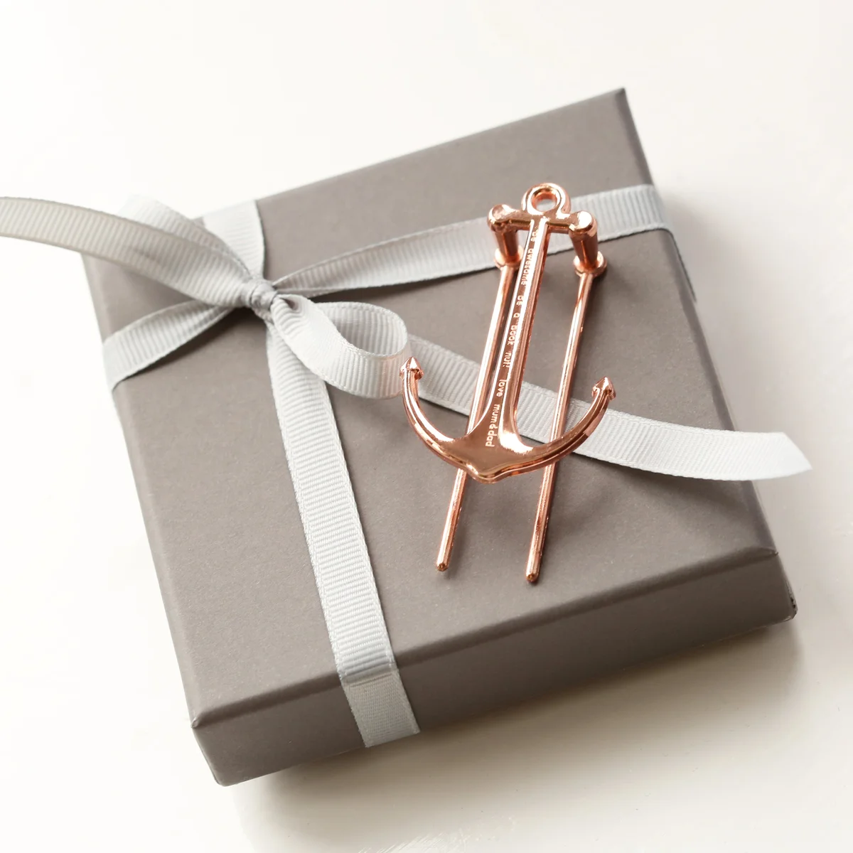 Gold and rose gold metal book anchor engraved with a message, displayed with a gift box on a white background