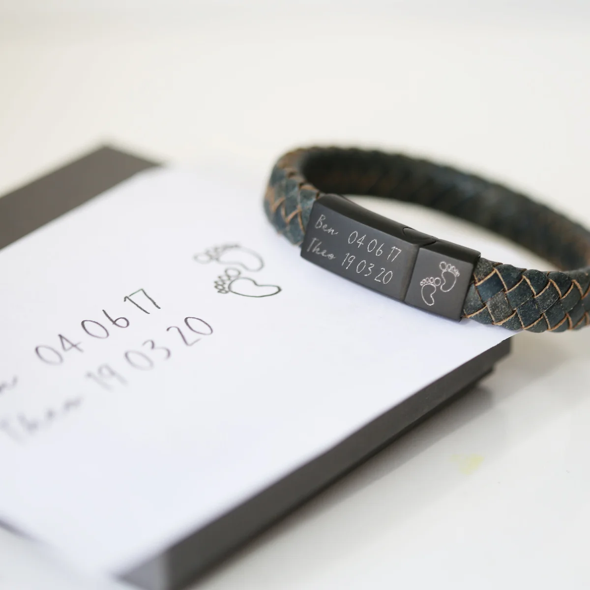 Close-up of iron leather magnetic snap lock bracelet with personalized handwriting engraving on woven strands