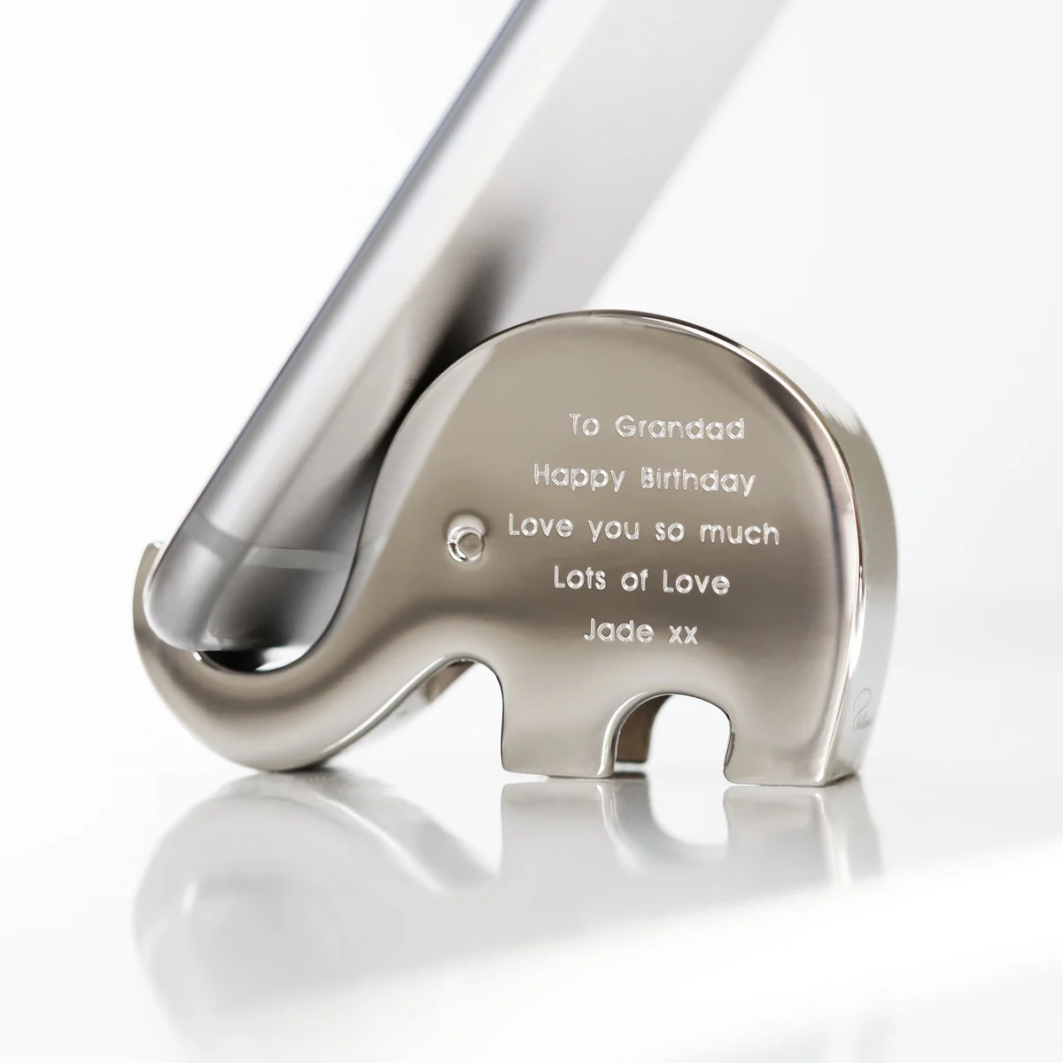Polished stainless steel elephant phone holder named Stampy balancing a phone on its trunk with engraved message