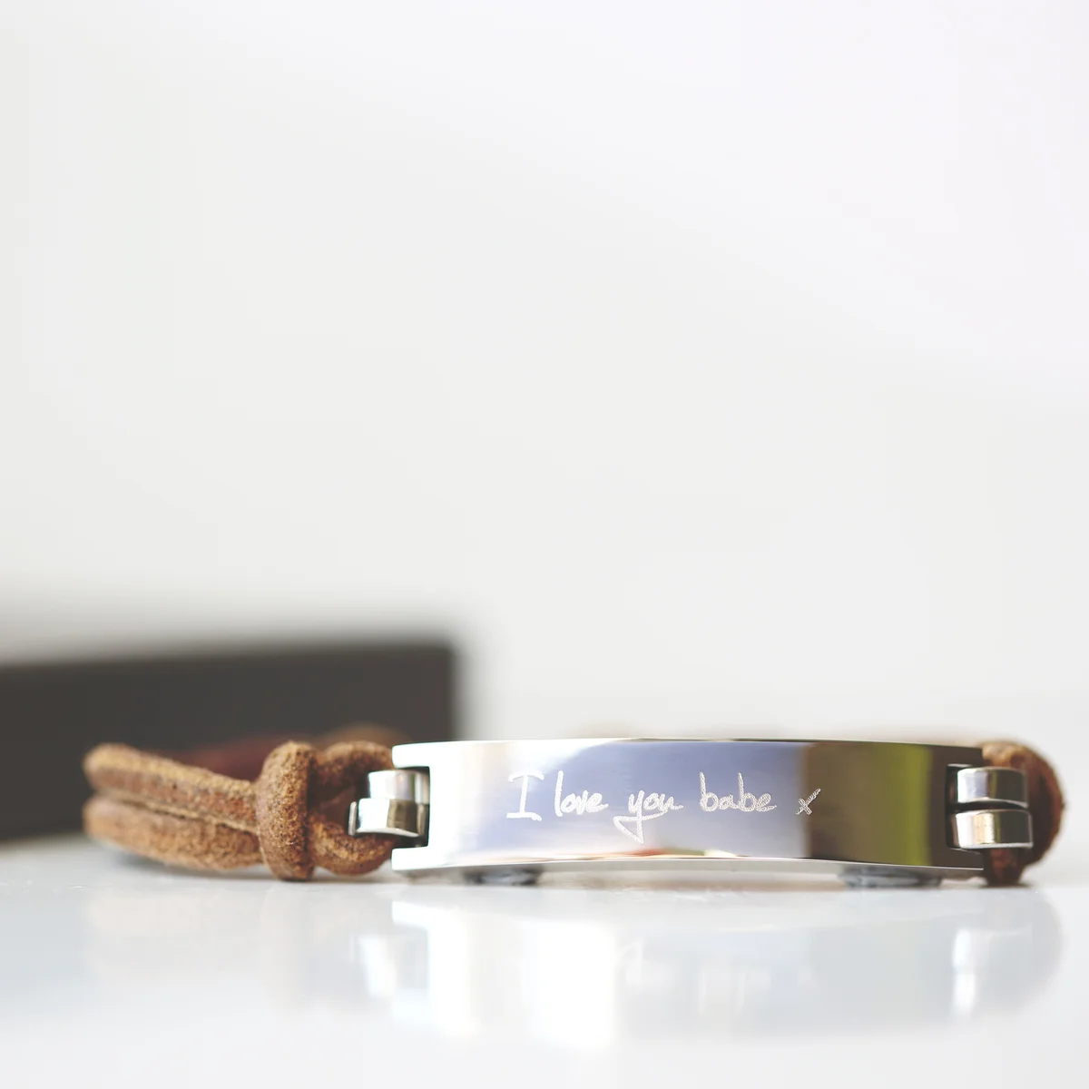 Tan leather bracelet with engraved handwriting on wide leather band and snap-lock clasp, shown on a white background