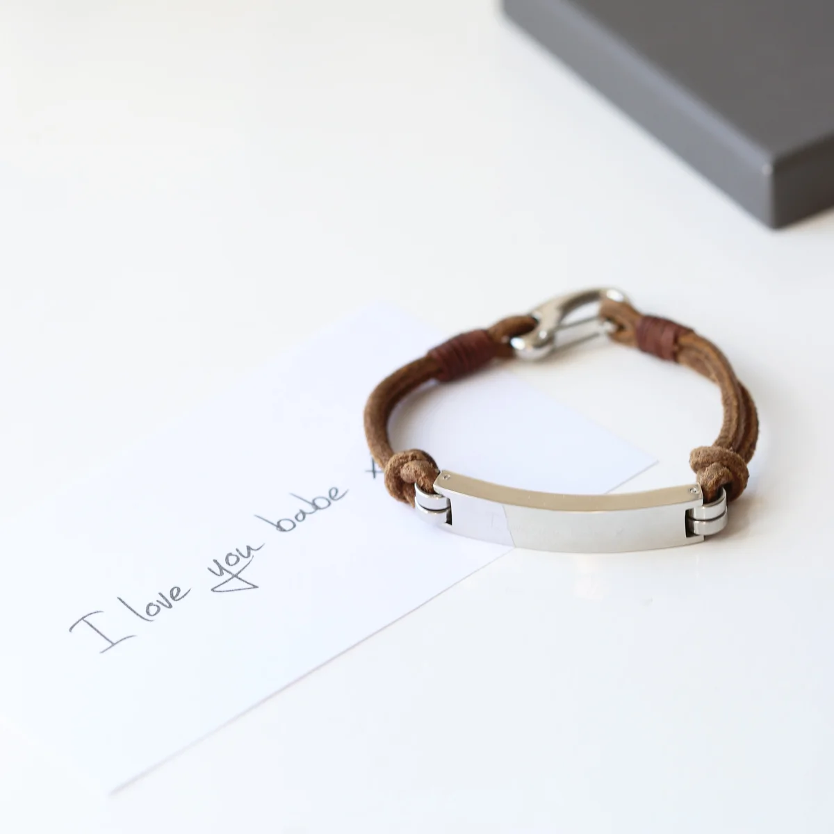 Tan snap-lock leather bracelet with engraved handwriting on wide leather strap, displayed on a white background