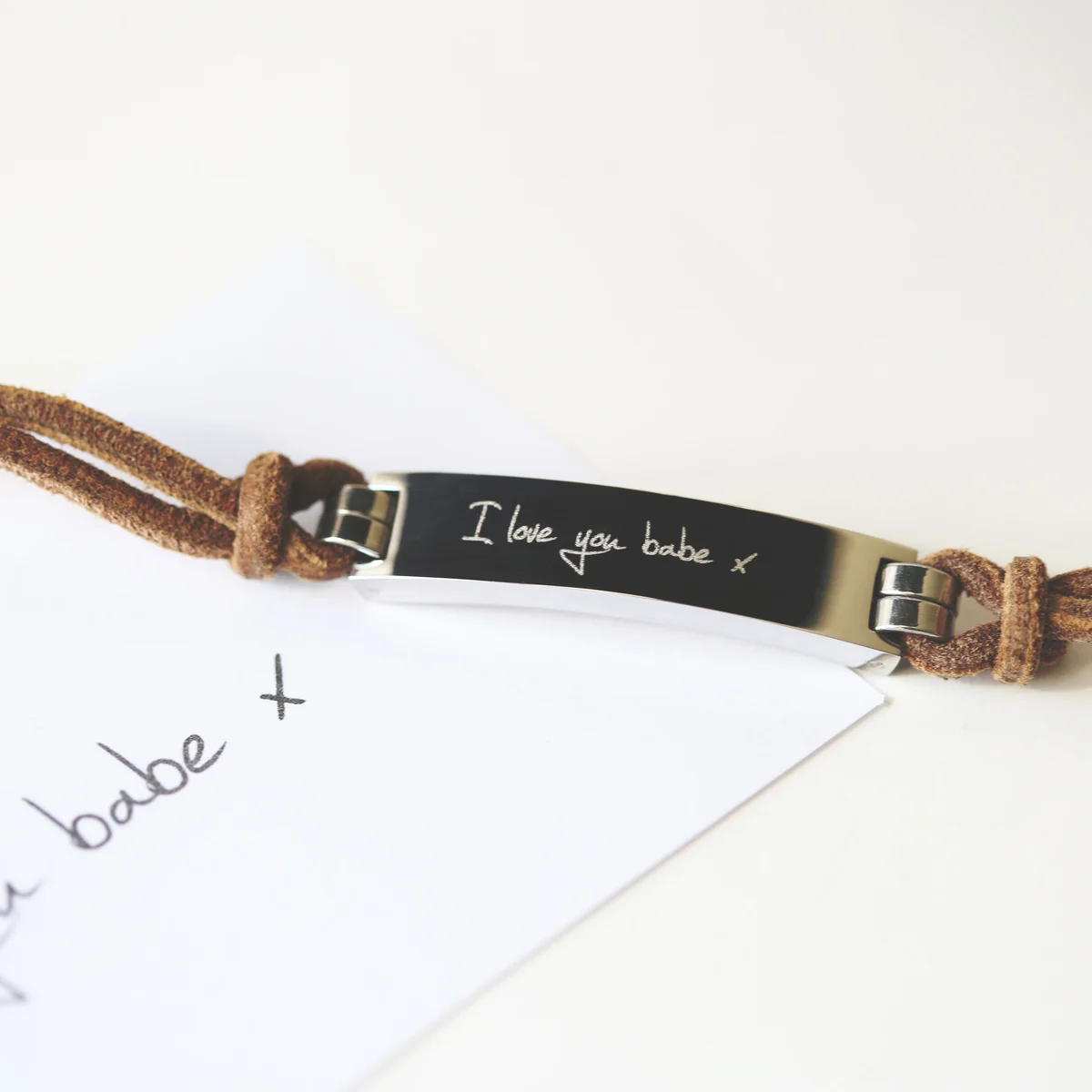 Tan genuine leather men's bracelet with engraved handwriting on wide central strip and snap-lock clasp on white background