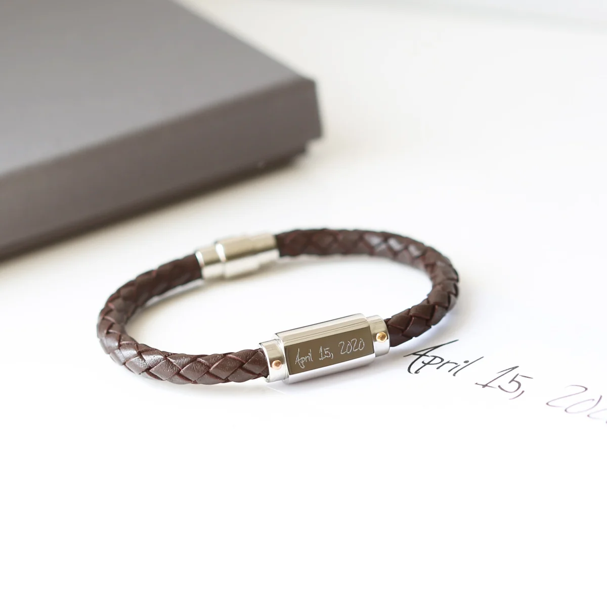 Close-up of a handwriting engraved bracelet with twisted black leather and magnetic snap-lock clasp on a white background