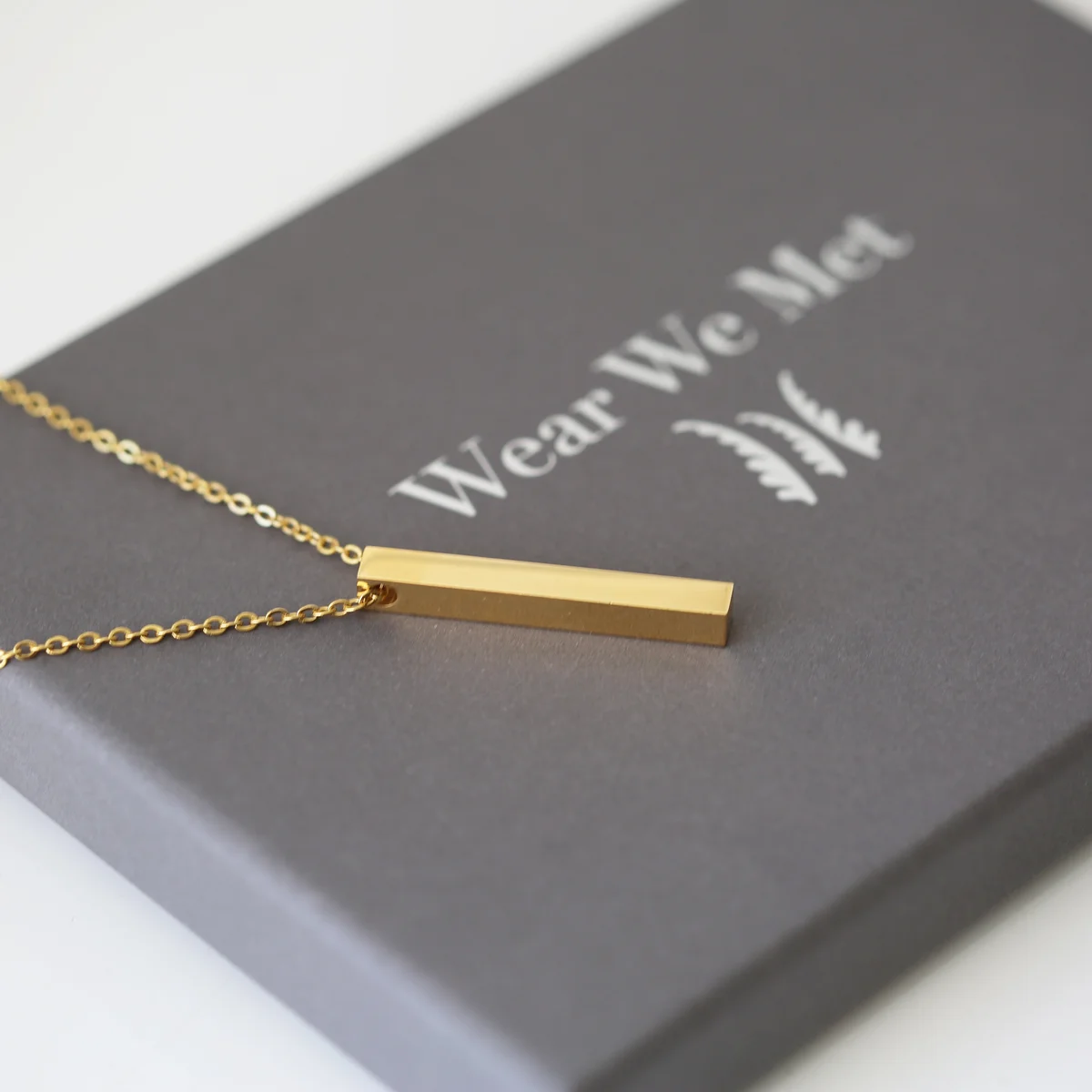 Delicate silver bar necklace engraved with modern font, displayed with gift box on white background