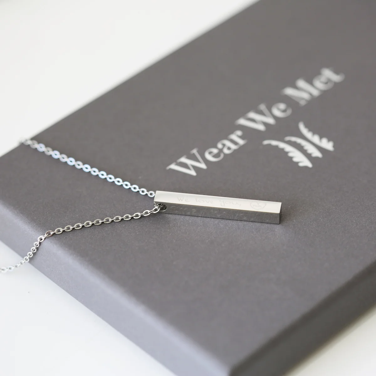 Rose gold necklace with a modern engraved bar pendant, displayed on a white background with a gift box nearby