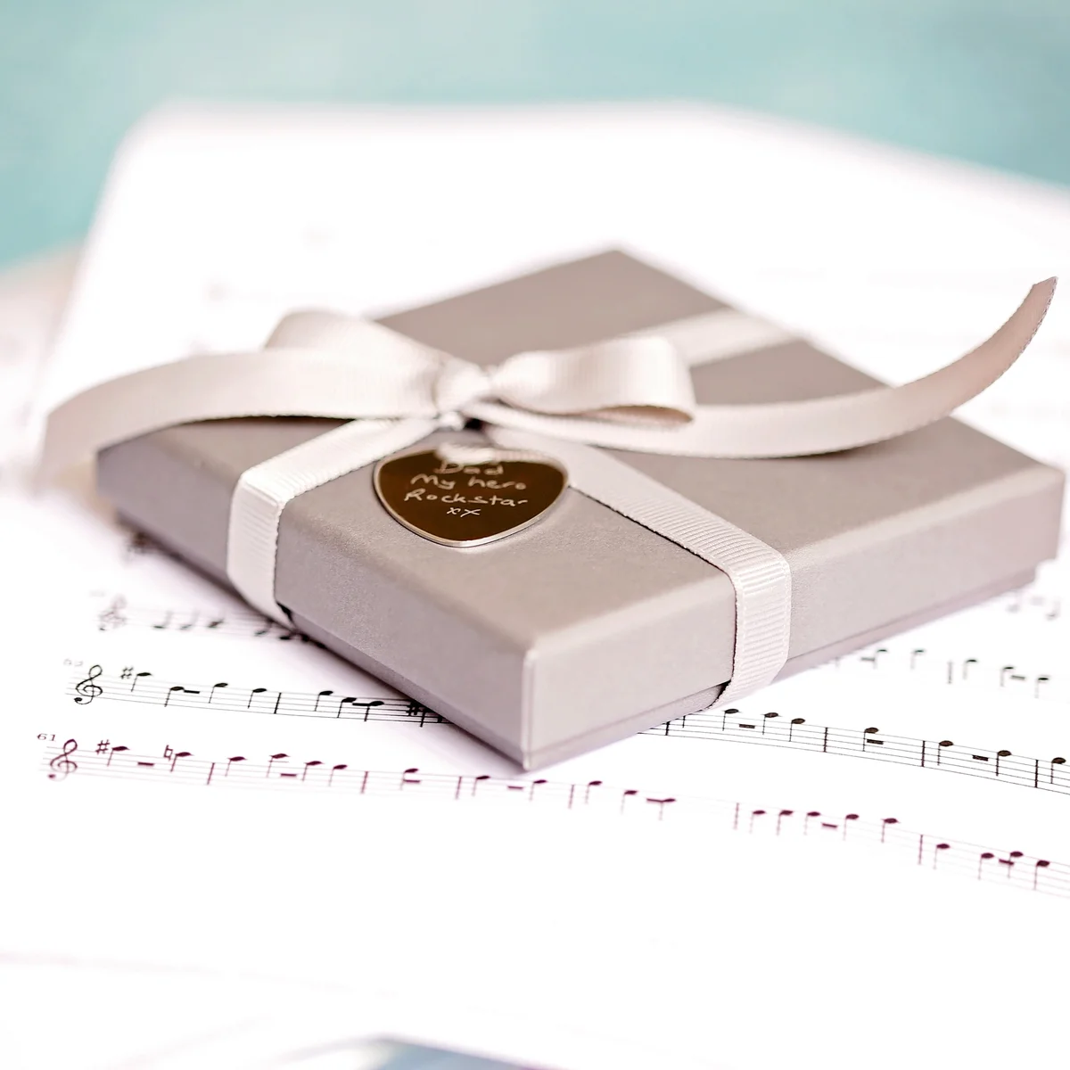 Polished stainless steel engraved guitar pick with custom handwriting, displayed in gift box with satin ribbon and blue shred