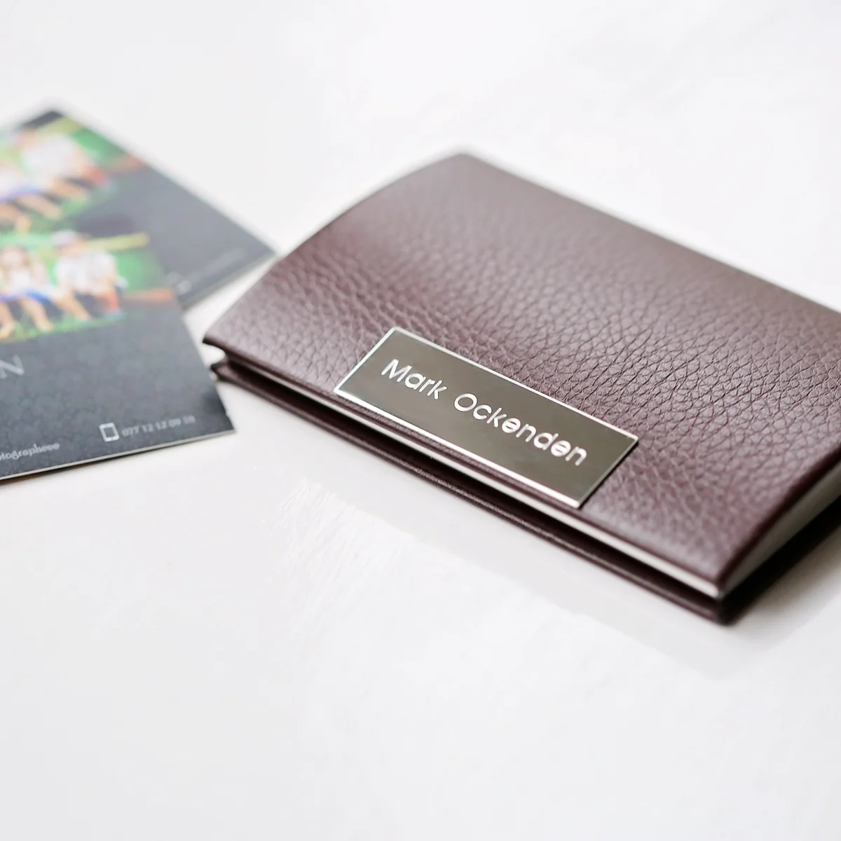 Engraved card holder in polished stainless steel with snap-lock closure, shown in black with personalized engraving area visible