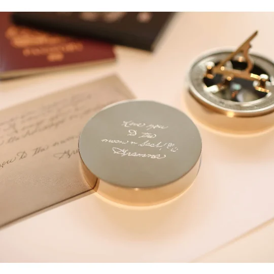 Engraved sundial compass with personalised handwriting on brass, shown next to protective pouch and gift box with ribbon
