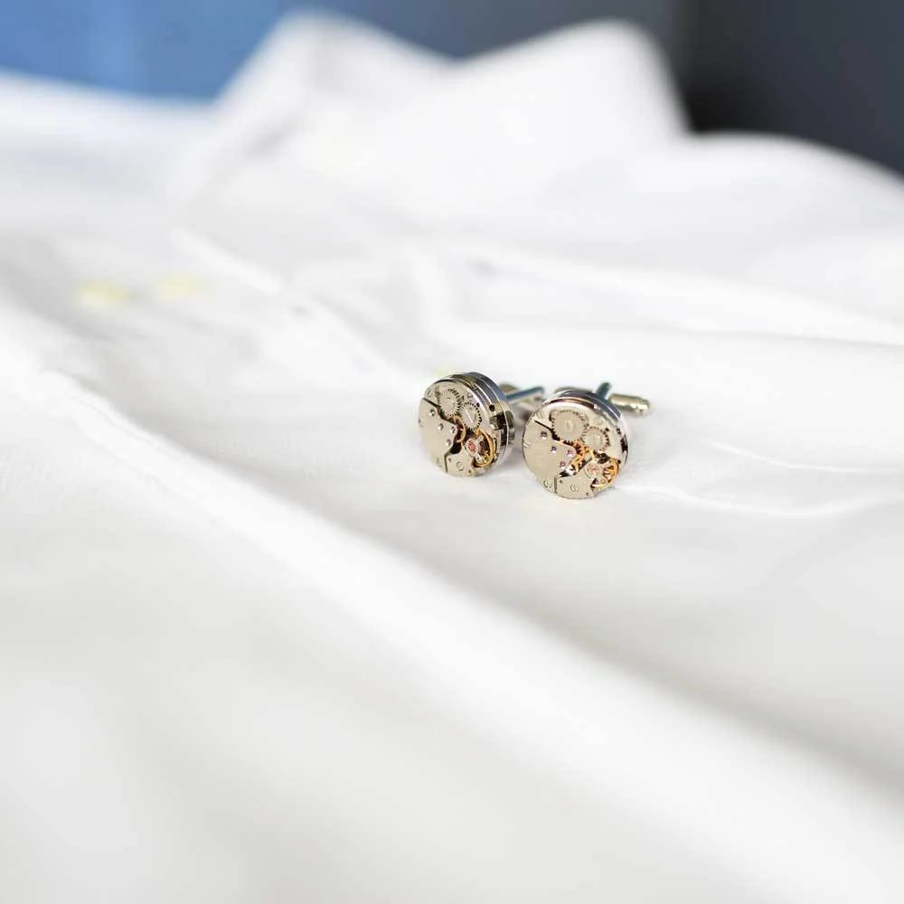 Pair of stainless steel cufflinks with visible moving gear mechanisms on a white background
